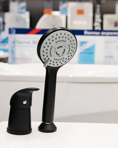 Closeup of black shower faucet in bathroom with transparent partition. Water flowing. Contemporary shower zone with rain head. Luxury house for sale